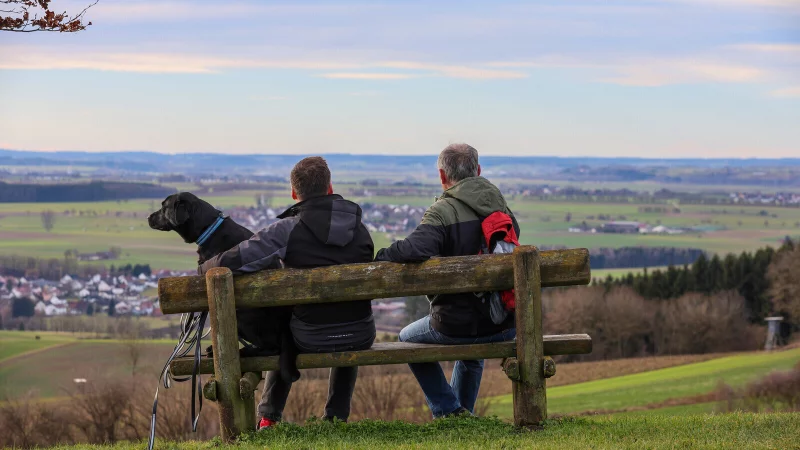 Wanderer sitzen mit einem Hund auf einer Bank am Waldrand. In den W&auml;ldern in OWL m&uuml;ssen immer wieder B&auml;nke abgebaut werden. - &copy; picture alliance/dpa