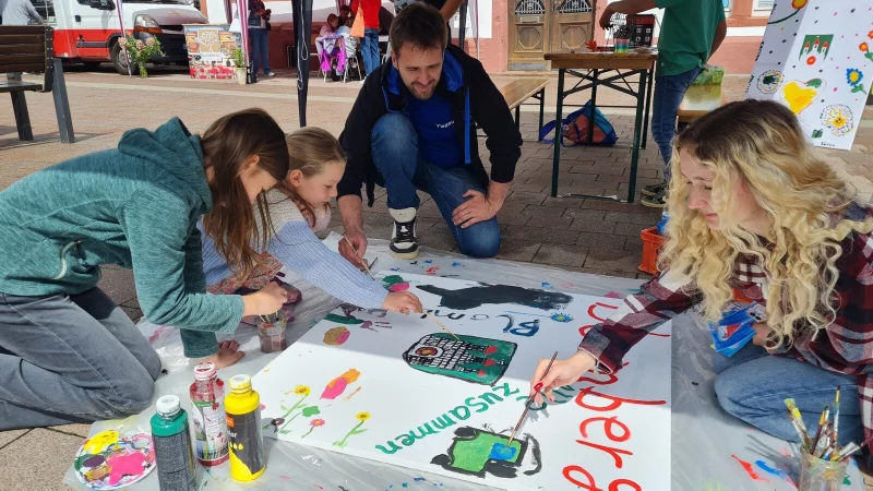 Junge Künstler auf dem Themenwochenmarkt zum Auftakt der Kunstmauer: Sozialpädagoge Sören Mellies (Mitte) und seine Kollegin Marleen Fürcht (rechts) freuen sich über die gute Resonanz. - © Marianne Schwarzer