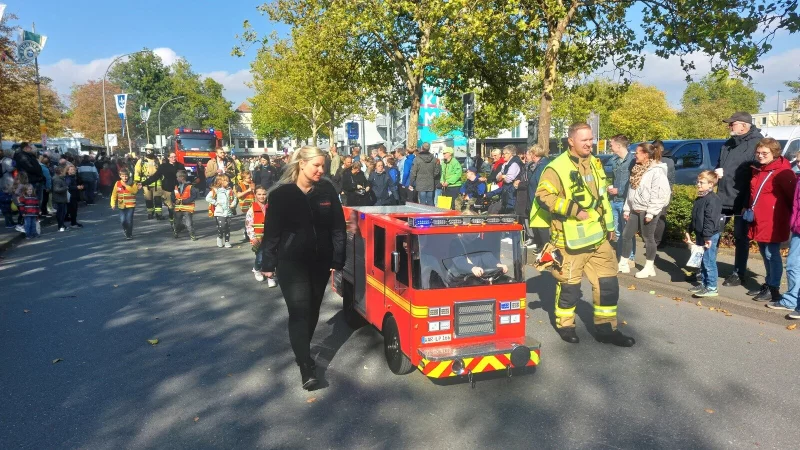 Im Festzug: Das Mini-Feuerwehrauto steuern Leni und Phil, die Eltern Janine und Maik Menne sichern links und rechts ab. - © Dieter Scholz