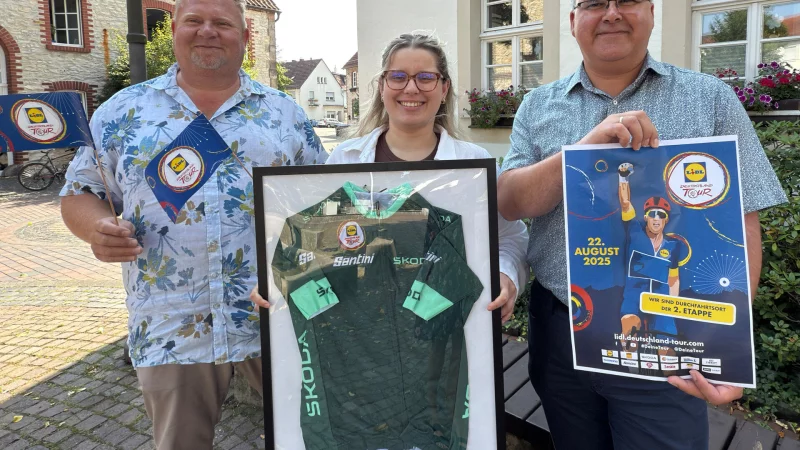 Mobilit&auml;tsmanager Henning Schwarze und B&uuml;rgermeister Marcus P&uuml;ster bereiten das Streckenfest vor und freuen sich, dass die Naturparkkommune Schlangen Etappenort ist. Auszubildende Michelle Geppert pr&auml;sentiert das Trikot von Radstar Jonathan Milan. - &copy; Gemeinde Schlangen