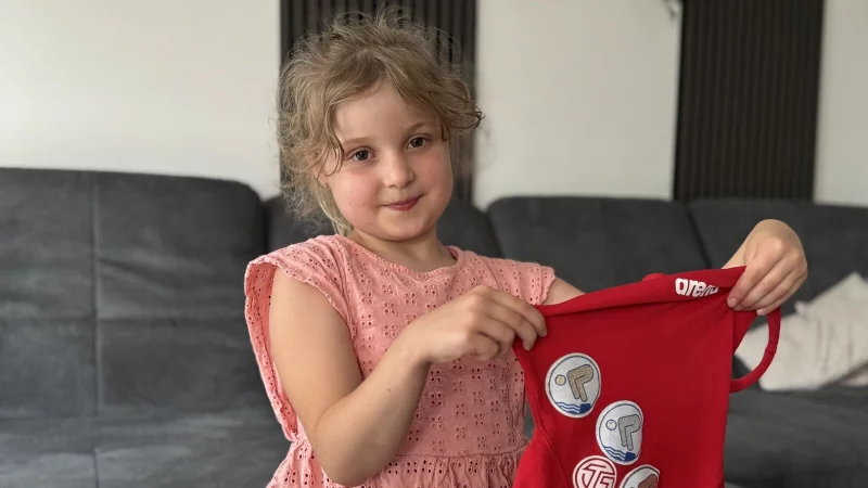 Tessa präsentiert stolz ihren roten Badeanzug mit den Schwimm-Abzeichen, die ihre Mama extra in der Glitzer-Variante aufgenäht hat. - © Sandra Castrup