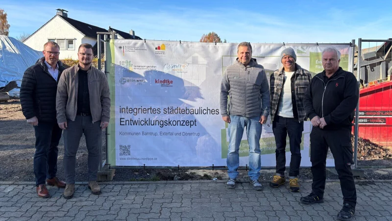 B&uuml;rgermeister Friso Veldink (von links), der zust&auml;ndige Sachbearbeiter Adrian L&uuml;cke, Oliver Brundiers (Gesch&auml;ftsf&uuml;hrer Gr&uuml;nwert OWL), Fachbereichsleiter Dirk S&uuml;llwold und Rolf Kledtke (Gesch&auml;ftsf&uuml;hrer Kledtke Elektro- und beleuchtungstechnik) stehen vor dem Bauzaunbanner mit der Umsetzungsplanung. Es fehlt Thekla Merfort vom Innovationszentrum D&ouml;rentrup. - &copy; Gemeinde D&ouml;rentrup