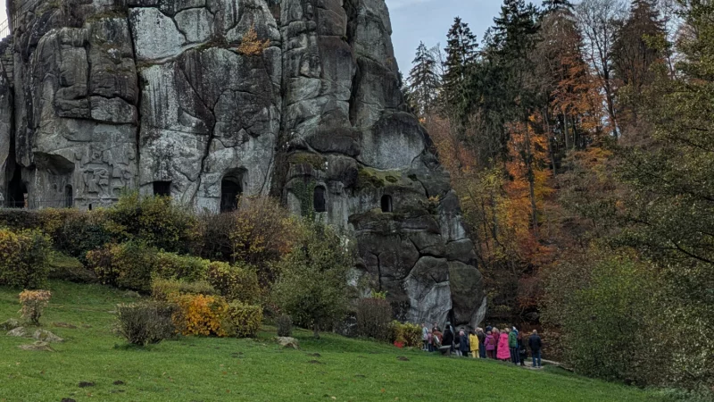 Bei herbstlicher Stimmung betrachtet eine Besuchergruppe das offene Felsengrab an den Externsteinen. - &copy; Landesverband Lippe