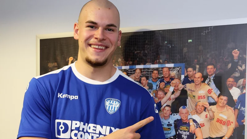 Jan Mudrow zeigt auf ein Foto, auf dem sein Vater Volker (stehend, Zweiter von rechts, neben Fynn Holpert) zu sehen ist. Es hängt in der Phoenix-Contact-Arena. Zu sehen ist das Lemgoer Meisterteam von 2003. - © Paul Cohen