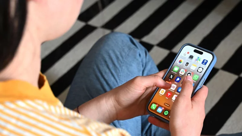 Eine junge Frau sitzt auf dem Boden und nutzt ein Smartphone – auf dem Display sind verschiedene Apps zu sehen. - © Elisa Schu/dpa