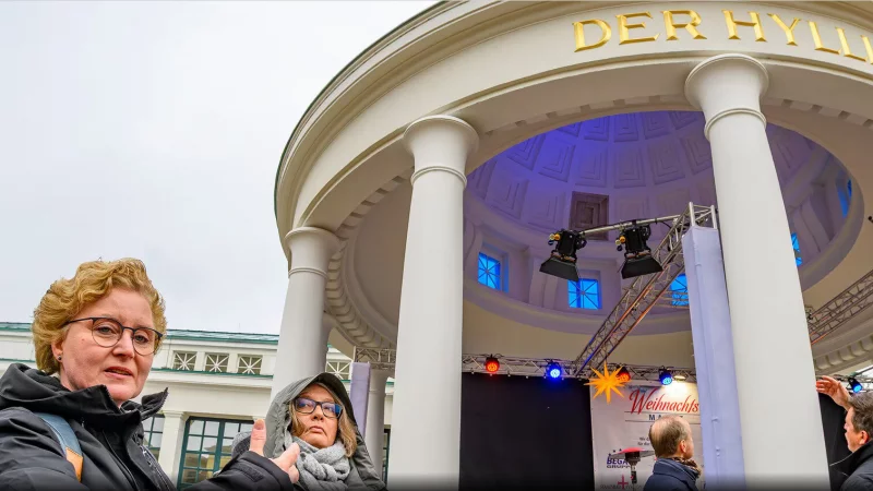Bauleiterin Stefanie Tünnermann (links) gibt einen Hinweis darauf, wie der frisch restaurierte Brunnentempel vor 100 Jahren aussah: "Damals gab es keinen Anstrich, sondern nur einen Muschelkalk-Putz", erklärt sie. Daran erinnert ein Feld ohne Farbe unter der Kuppel. - © Carlhermann Schmitt