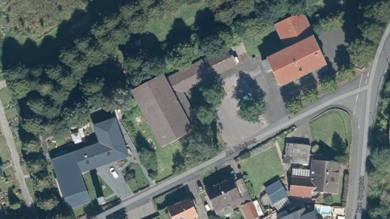 Die Stra&szlig;e "Am Schulweg" in Ahmsen aus der Vogelperspektive. Der neue Dorfplatz soll zwischen dem Dorfgemeinschaftshaus (rechts oben) und der Turnhalle (Bildmitte) entstehen. Hinter dem Dorfgemeinschaftshaus befindet sich weiterer Parkraum f&uuml;r Autos (ganz rechts). - &copy; TIM-online/Geobasisdaten NRW