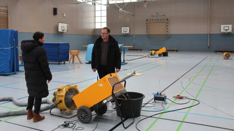 In der Turnhalle der Karla-Raveh-Gesamtschule laufen die Trocknungsger&auml;te. &Uuml;ber die Situation tauschen sich die Karen Zereike (links, Leiterin des Eigenbetriebs Schulen des Kreises Lippe) und Geb&auml;udetechniker Matthias Metting aus. - &copy; Till Brand