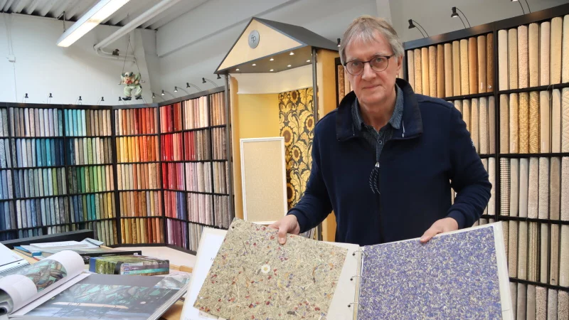 Gert Pr&uuml;&szlig;ner steht in seinem Teppichboden-Studio und bl&auml;ttert am Kollektionstisch durch verschiedene Tapetenmotive. Neben den beliebten Digitaldruck-Fototapeten sind besonders die duftenden Tapeten aus &Ouml;sterreich ein Hingucker &ndash; ihre Oberfl&auml;chen bestehen aus getrocknetem Heu oder Kornblumen. Foto: Anna Lena Hinder - &copy; Anna Lena Hinder