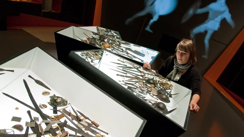 Unser Archivbild aus 2009 zeigt Ausstellungsmitarbeiterin Caroline Koch im Varusschlachtmuseum in Bramsche-Kalkriese (Landkreis Osnabrück). In der Vitrine sind Waffenopfer aus dem dänischen Illerup zu sehen. Das Museum widmet sich in seiner Sonderausstellung "Konflikt" den Kriegen in der germanischen Welt nach der Varusschlacht. Mehrere tausend archäologische Exponate aus ganz Europa sind für die Schau zusammengetragen worden. - © dpa