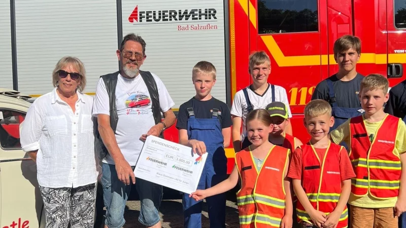 Oldtimer-Fan Klaus Siekmann übergibt einen symbolischen Spendenscheck an die Gruppe 1 der Jugendfeuerwehr Holzhausen. Links steht Siekmanns Lebensgefährtin Petra Werner. - © Klaus Siekmann