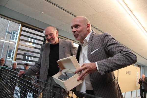 Geschenk für den Ruhestand: Zur Ausstellungseröffnung übergibt Dekan Carsten Wiewiorra (rechts) Prof. Reinhold Tobey einen Bronzebarren, weil er sich auch mit Gusstechnik beschäftigt hat. Die Beiden stehen auf einem von Tobey entworfenen Balkon. - © Marianne Schwarzer