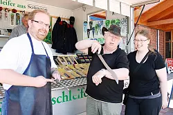 Dass im Sortiment von Scheren-Schleifer Guido Morsbach (links) alles scharf ist, davon überzeugt sich Rainer Wiesner an seinen Arm-Härchen. Tochter Melissa schaut zu. - © Foto: Castrup