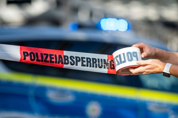 Ein Absperrband wird vor einem Polizeiwagen ausgerollt. - © David Inderlied/dpa/Illustration