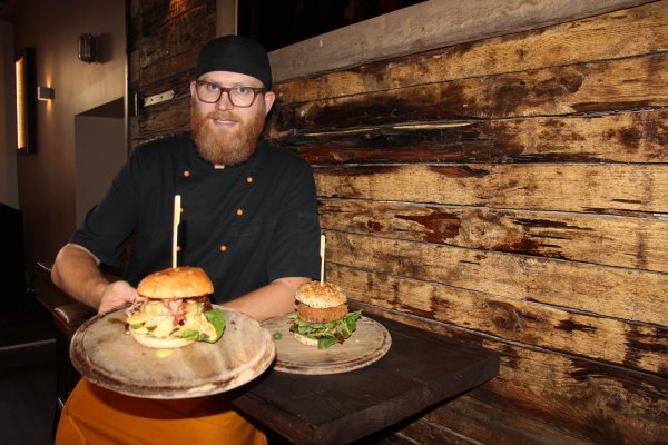 Sebastian Schraets präsentiert zwei Kreationen: Der eine Burger besteht aus einem vegetarischen Süßkartoffel-Walnuss-Bratling, getrockneten Tomaten und Büffelmozzarella, der andere aus Rindfleischpatty, Speck, Honig und Käsesauce. - © Kirsten Fuhrmann