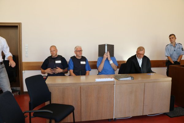 Andreas V. hält sich einen Aktenordner vors Gesicht. Auf seinen Armen sind Spuren einer Verletzung zu sehen. - © Kateryna Akulenko