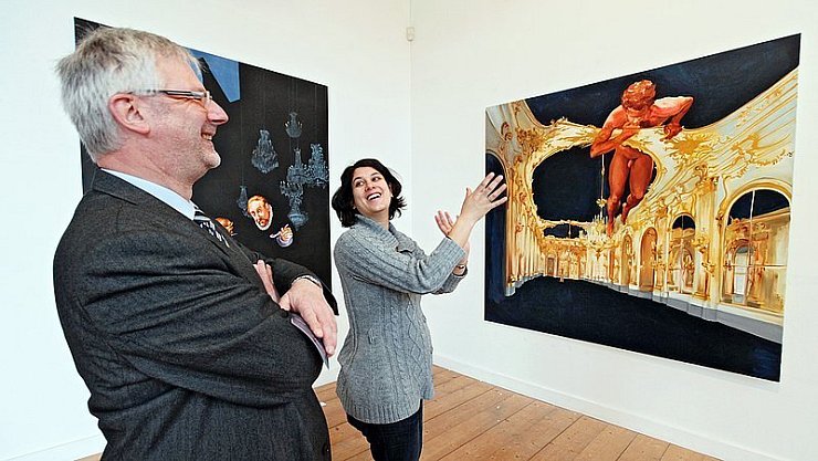 Üppig und opulent: So kommen die Gemälde von Sala Lieber daher, die Dr. Mayarí Granados hier gemeinsam mit dem Bürgermeister der Stadt Schieder-Schwalenberg, Gert Klaus, im Robert-Koepke-Haus bewundert. - © Foto: Gerstendorf-Welle