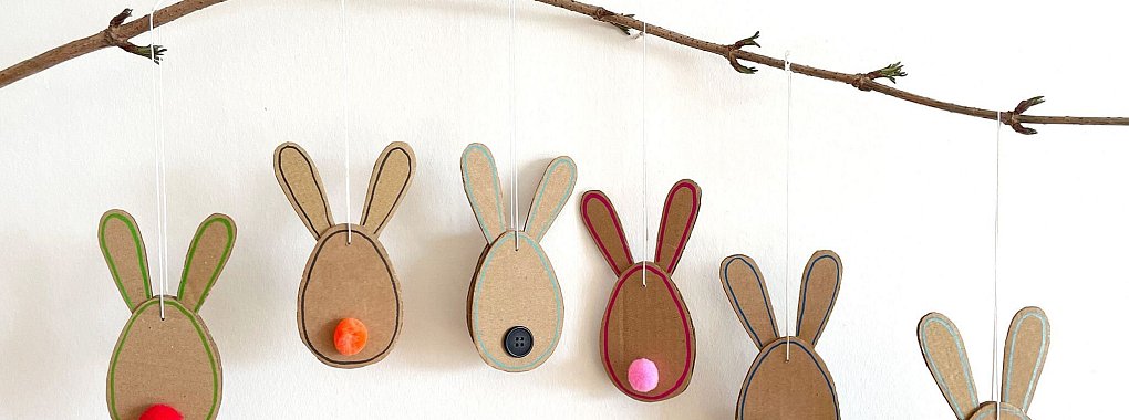 Schnelle Hasen: Aus einem unbedruckten Versandkarton und bunten Bommeln entstehen schöne Osteranhänger. - © DIY Academy/dpa-tmn