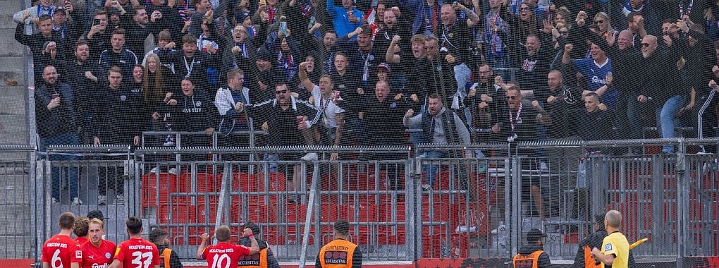 Die Spieler von Holstein Kiel freuen sich mit ihren Fans über einen unerwarteten Punkt bei Bayer Leverkusen. - © Rolf Vennenbernd/dpa