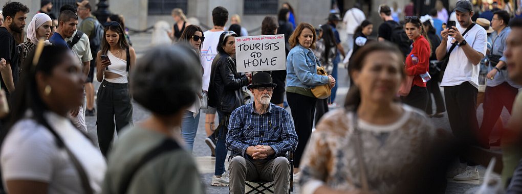Barcelona im November 2024: Ein Aktivist auf dem Plaza de Sant Jaume in Barcelona zeigt ein Schild mit der Aufschrift 'Tourists go home''. - © picture alliance / NurPhoto