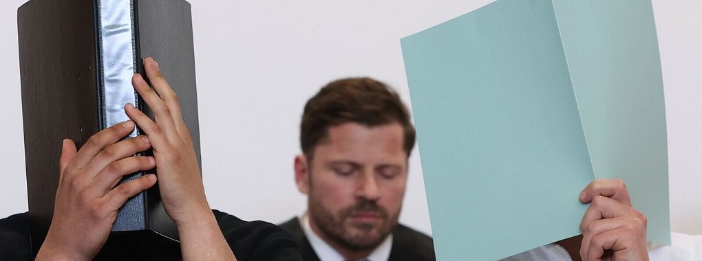Der Hauptangeklagte (r) sitzt in einem Gerichtssaal neben weiteren Angeklagten vor Rechtsanwalt Harald Stehr (M) auf der Anklagebank. Der Mann wurde wegen eines Böllerwurfs mit zwölf Verletzten zu einer Gefängnisstrafe verurteilt, das Urteil ist nun rechtskräftig. (Archivbild) - © Karl-Josef Hildenbrand/dpa