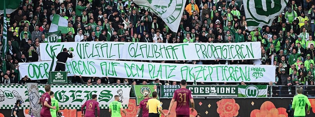 Wolfsburgs Fans mit einem Banner mit der Aufschrift «VfL Vielfalt glaubhaft propagieren - oder Behrens auf dem Platz akzeptieren». - © Swen Pförtner/dpa