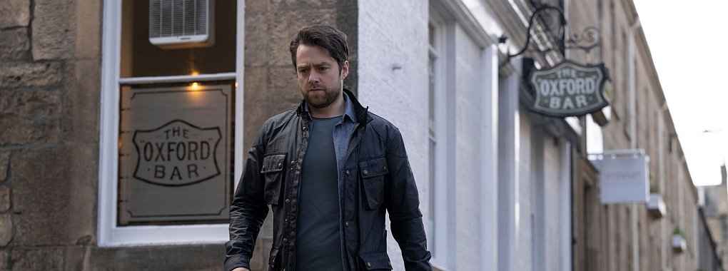 Richard Rankin spielt John Rebus, einen Kriminalkommissar mit sehr eigenwilligem Stil, der sich ungern an Konventionen und Höflichkeiten hält. - © Graeme Hunter Pictures/Magenta TV+/dpa