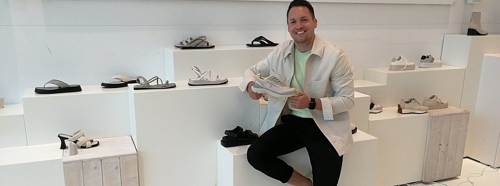 Jonas Gurcke im Showroom von Wortmann. Hier werden die neuen Modelle besprochen und vorgestellt. Im Hintergrund sind die neuen Sandalen der Premium-Kollektion "Newd.Tamaris." zu sehen. In der Hand hält Jonas Gurcke sein neues Liebliengsstück aus der Outdoor-Kollektion. - © Freya Köhring