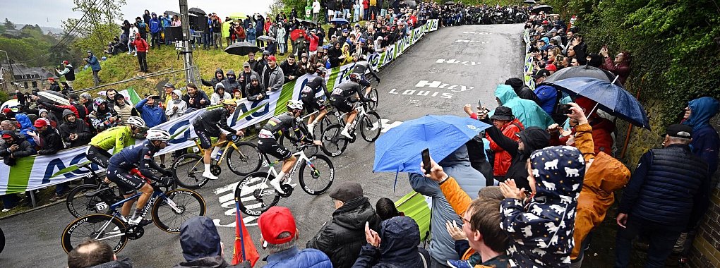 Olympiasieger Remco Evenepoel (M) mit goldenem Helm an der Mauer von Huy. Rechts neben ihm Tadej Pogacar. - © Jasper Jacobs/Belga/dpa