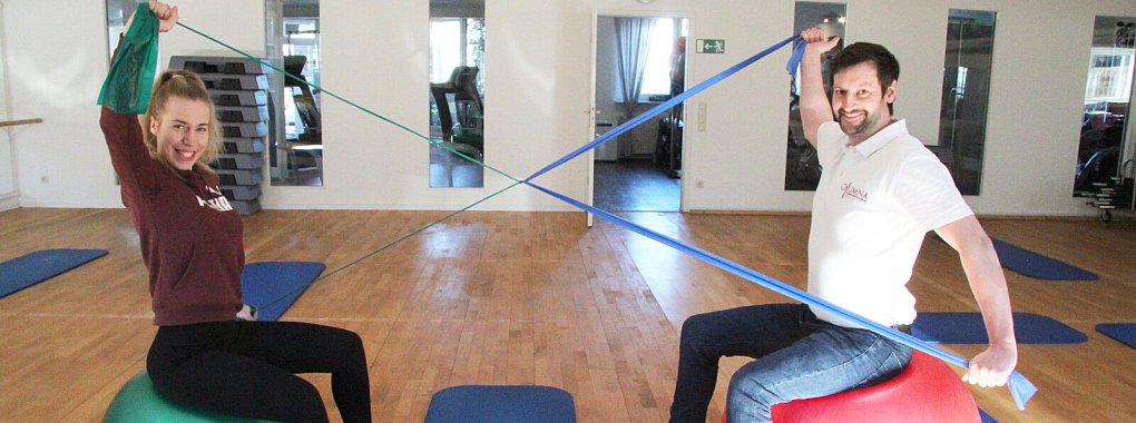 Jacqueline Schöne und Daniel Paier zeigen eine Übung zur Aufrichtung der Brustwirbelsäule. Dazu braucht man ein Theraband, idealerweise einen Sitzball, sowie - falls man keinen Übungspartner hat - eine Stelle, um das Theraband zu fixieren. Das wird dann mit den Händen so weit wie möglich Richtung Rücken geführt - mal höher, mal niedriger, mal mit gestreckten, mal mit angewinkelten Armen. - © Dieter Asbrock