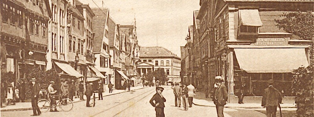 Um das Jahr 1900 stehen etliche Detmolder auf der Langen Straße an der Kreuzung zur Exterstraße. Im Hintergrund ist das neue Rathaus zu sehen, links der Eingang zur Gastronomie „Arminiushalle". - © Stadtarchiv Detmold