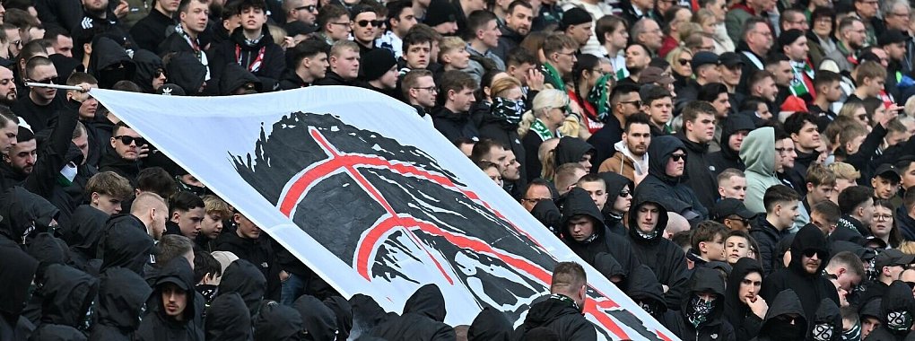 Hannover-Fans halten auf der Tribüne ein Plakat hoch, dass den Kopf von Niedersachsens Innenministerin Daniela Behrens in einem Fadenkreuz zeigt. - © Swen Pförtner/dpa