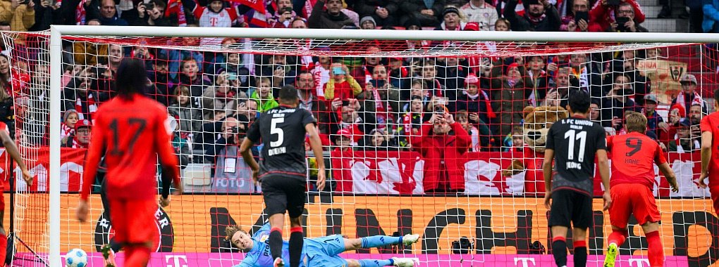 Harry Kane (r) schießt den Elfmeter in die Ecke, die ihm Union-Torwart Frederik Rönnow anzeigte. - © Tom Weller/dpa