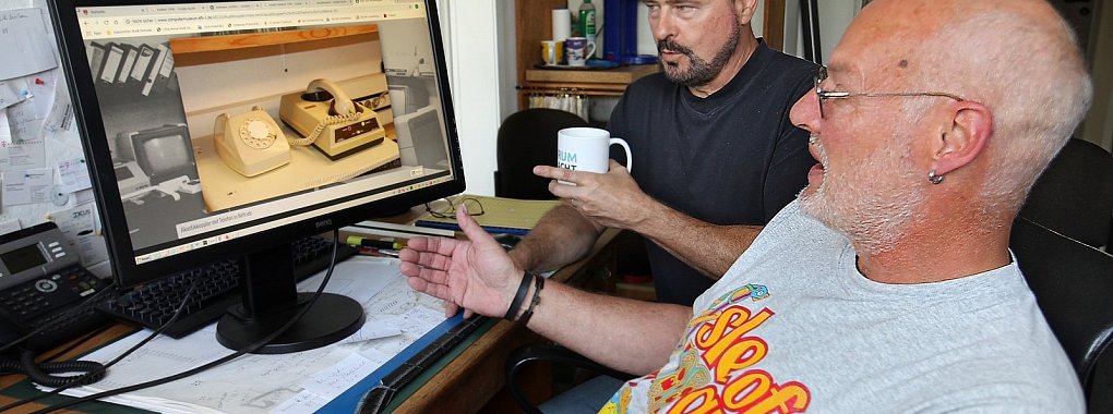Ulrich Stephanides (hinten) und André Gronemeier amüsieren sich über ein Bild, das einen Akustikkoppler zeigt, mit dem die in Töne verwandelten Daten vom Rechner per Telefon ins Internet gelangten. - © Bernhard Preuß