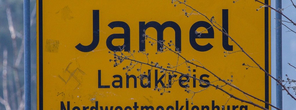 Ein Hakenkreuz ist auf dem Ortseingangsschild der kleinen Ortschaft Jamel zu sehen. Über das Festival «Jamel rockt den Förster» gegen Rechtsextremismus in dem Dorf gibt es jetzt eine Doku in der ARD-Mediathrek. - © Jens Büttner/dpa