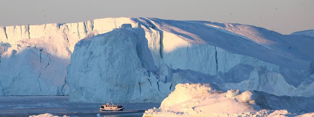 Ein Schiff mit Touristen fährt im Ilulissat-Eisfjord im Westen von Grönland an Eisbergen vorbei. - © Steffen Trumpf/dpa-tmn