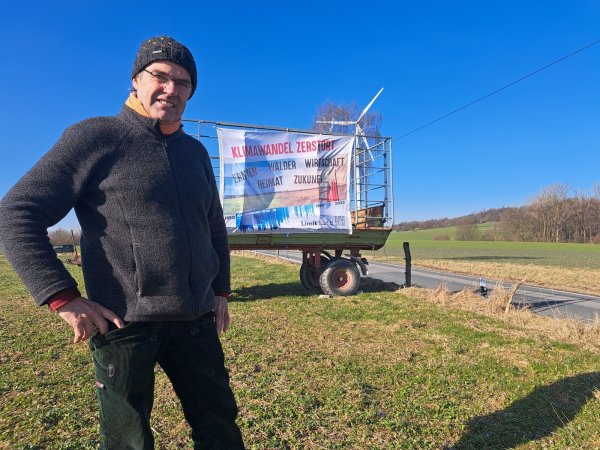Ulf Allhoff-Cramer vor einem Plakat, das auf die Zerstörung durch den Klimawandel aufmerksam macht. - © Carolin Brokmann-Förster