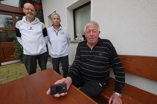 Thomas Trachte (von links), Sonja Schröder und Fritz Hilmert zeigen den winzigen Mobilfunk-Hotspot, den die Telekom jedem Haushalt als Ersatz-Internetzugang zur Verfügung gestellt hat. Dumm nur, dass in Mosebeck so schlechter Mobilfunkempfang ist, dass der Router kaum etwas nützt. - © Jost Wolf