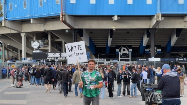 Thomas Melchior hält am vergangenen Freitag sein "Wette verloren"-Schild vor der Bielefelder Schüco-Arena in die Höhe. Dahinter reihen sich die Arminia-Fans in die Schlange ein, um rechtzeitig zum Spiel gegen den 1. FC Magdeburg ins Stadion zu kommen. - © privat