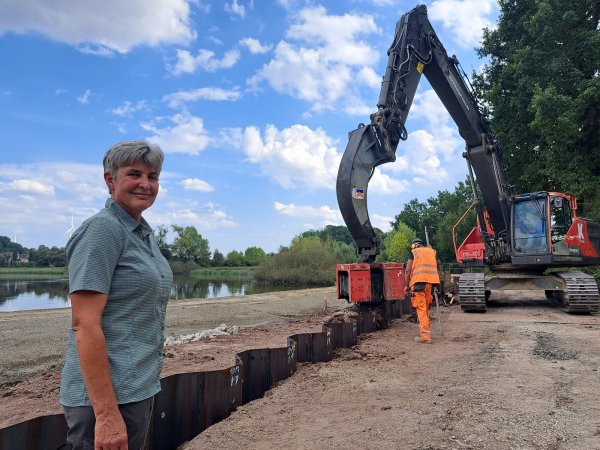 Susanne Hoffmann, stellvertretende Leiterin der Forstabteilung des Landesverbands Lippe, begleitet die Arbeiten am Norderteich. Im Hintergrund bringen Mitarbeiter der Firma Kögel die Spundwandelemente mit schwerem Gerät in den Boden ein. - © Carolin Brokmann-Förster
