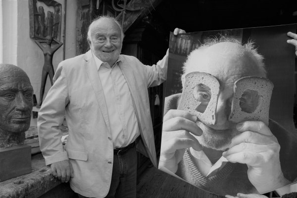 Bruno Buschmann ist für jeden Spaß zu haben gewesen. Auf dem großformatigen Bild neben ihm blickt der Bildhauer in seinem Oerlinghauser Atelier durch eine 90, die aus zwei Brotscheiben ausgeschnitten worden ist. - © Karin Prignitz