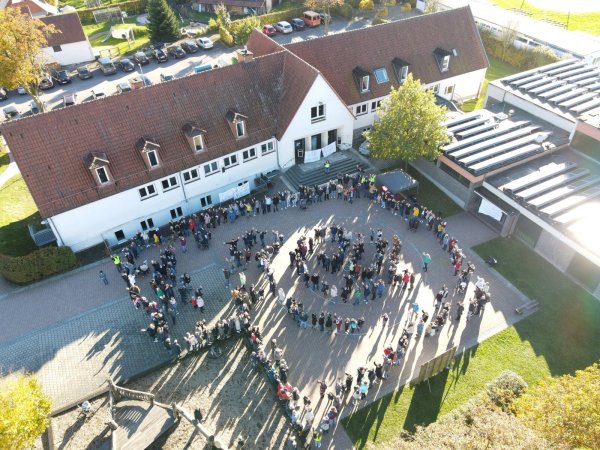 Mit einer Menschenkette umrahmen die Gegner der Schulschließung in Alverdissen das Gebäude. Aus der Luft macht eine Drohne Aufnahmen. - © Sylvia Frevert