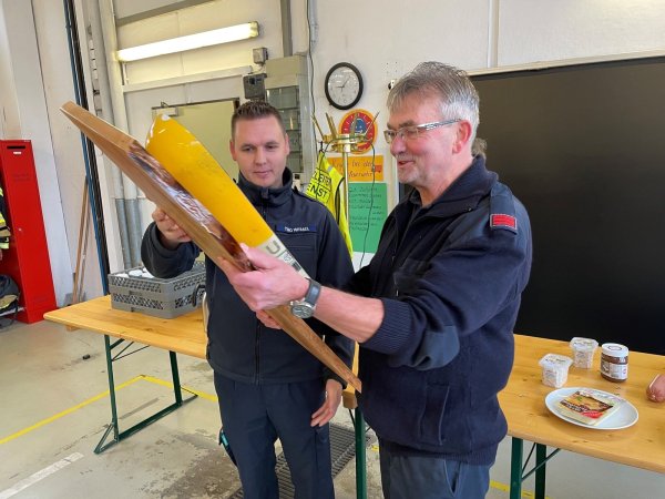 Der Leiter Atemschutz der Freiwilligen Feuerwehr Bad Salzuflen, Timo Wessel (links), überreicht Willi Schmidtpott als Geschenk eine speziell präparierte Atemluftflasche. - © Daniel Hobein / Feuerwehr Bad Salzuflen