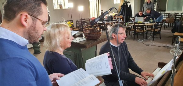 Vikar Gregor Block (von links), Pastorin Bettina Hanke-Postma und Superintendent Holger Postma proben für den ersten Online-Gottesdienst. Im Hintergrund ist das Technik-Team um Social-Media-Pfarrer Wolfgang Loest mit der Technik beschäftigt, die zwei Tische beansprucht. - © Uwe Rotkamp