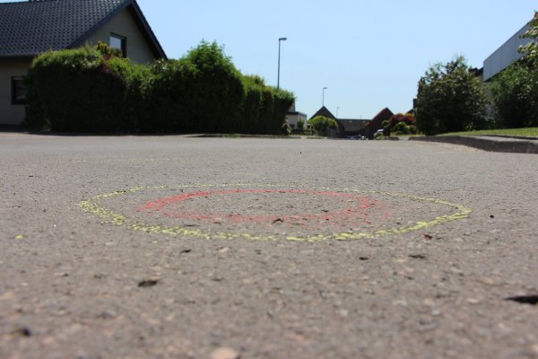 Mehr als 30 gelb-rot markierte Kreise (das Bild zeigt einen davon) auf der Straßendecke in der Salzufler Sackgasse deuten genau auf die Stellen hin, wo die Spurensicherung am Einsatzort Patronenhülsen sichergestellt hat. Fünf Kugeln trafen den immer noch schwer verletzten 19-jährigen Fahrer. - © Janet König