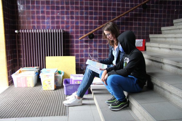 Konrektorin Gesine Hille sitzt mit einem Schüler auf der Treppe am Eingang und erklärt eine Aufgabe für die Woche. - © Jana Beckmann