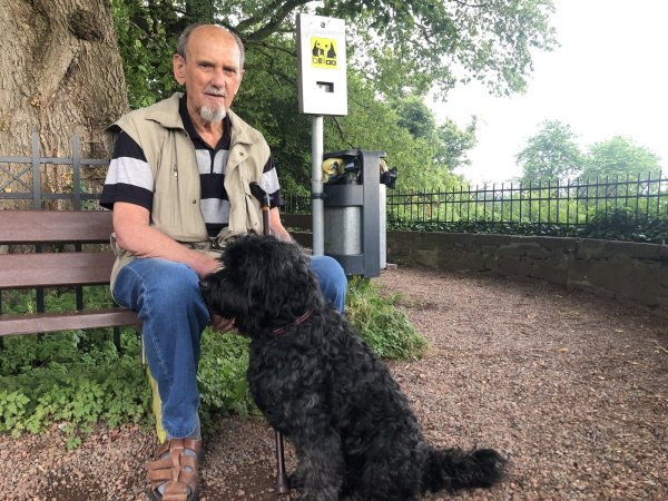 Horst Frunzke sitzt mit seinem Hund „Donald“ auf einer Bank, neben der ein Kotbeutel-Spender angebracht ist. - © Silke Buhrmester