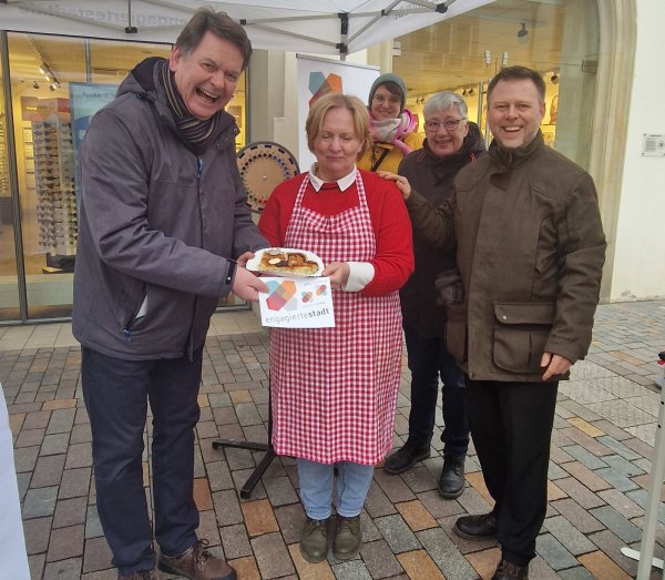 Am Infostand freuten sich Jochen Beuckers (links, Sprecher der Engagierten Stadt NRW) und Hendric Schwär-Fröhlich (rechts, persönlicher Referent des Bürgermeisters) über einen Gruß von Annette Diekmann vom Pickert-Mädel-Stand auf dem Wochenmarkt. - © Stadt Lemgo