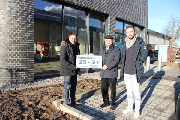 Architekt Nils Duderstadt (links) überreicht Investor Günther Brandt die Hausnummer des Neubaus. Dieser steht an der Lageschen Straße 25-27. Philipp Schmidt von der zuständigen Baufirma hat den Bau begleitet. Im Hintergrund zieht bald Subway ein. Im Gebäudeteil dahinter Jysk. - © Kirsten Fuhrmann