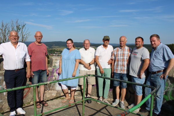 Klaus Meier (von links), Axel Kunze, Yvonne Eisenhauer, Ulrich Kollekowski, Wolfgang Blome, Jürgen Müller, Bastian Homuth und Matthias Müller zeigen auf dem Windmühlenstumpf, welche Beeinträchtigungen sie durch die drei Anlagen befürchten. Im Hintergrund ist Sonneborn zu sehen. - © Lorraine Brinkmann